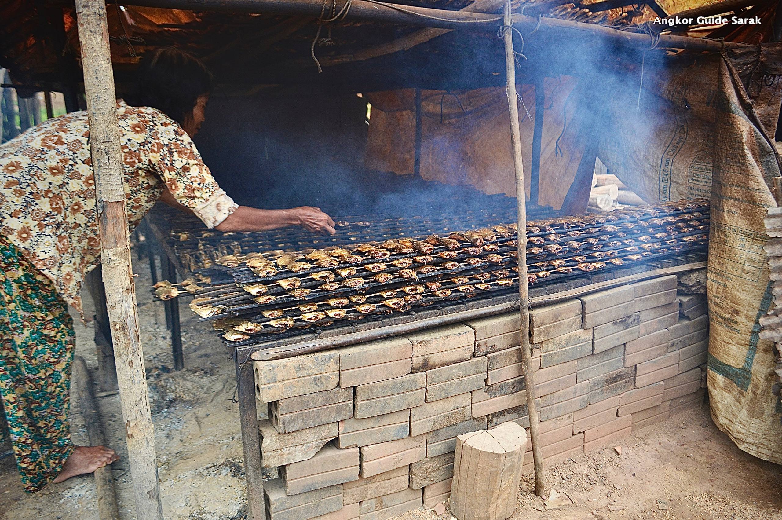 An elderly woman making smoked fish using traditional Cambodian methods.