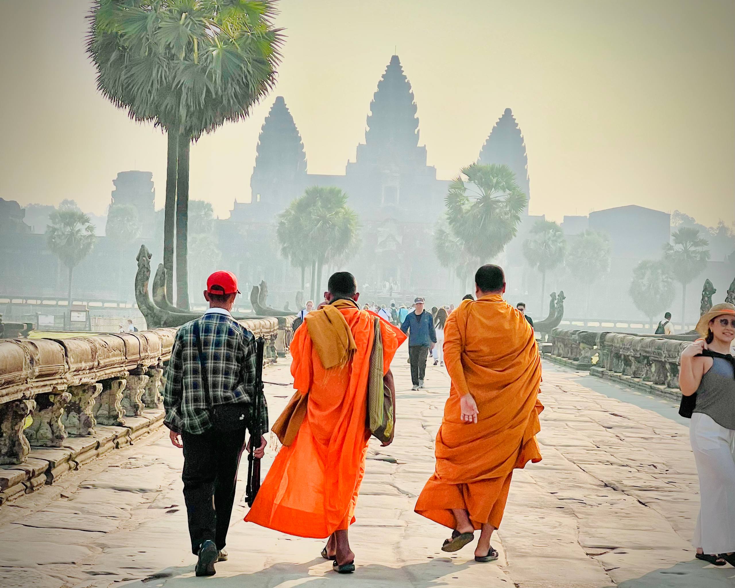 Buddhist monks and local visitors walk across the ancient causeway toward Angkor Wat in the soft morning light of sunrise.