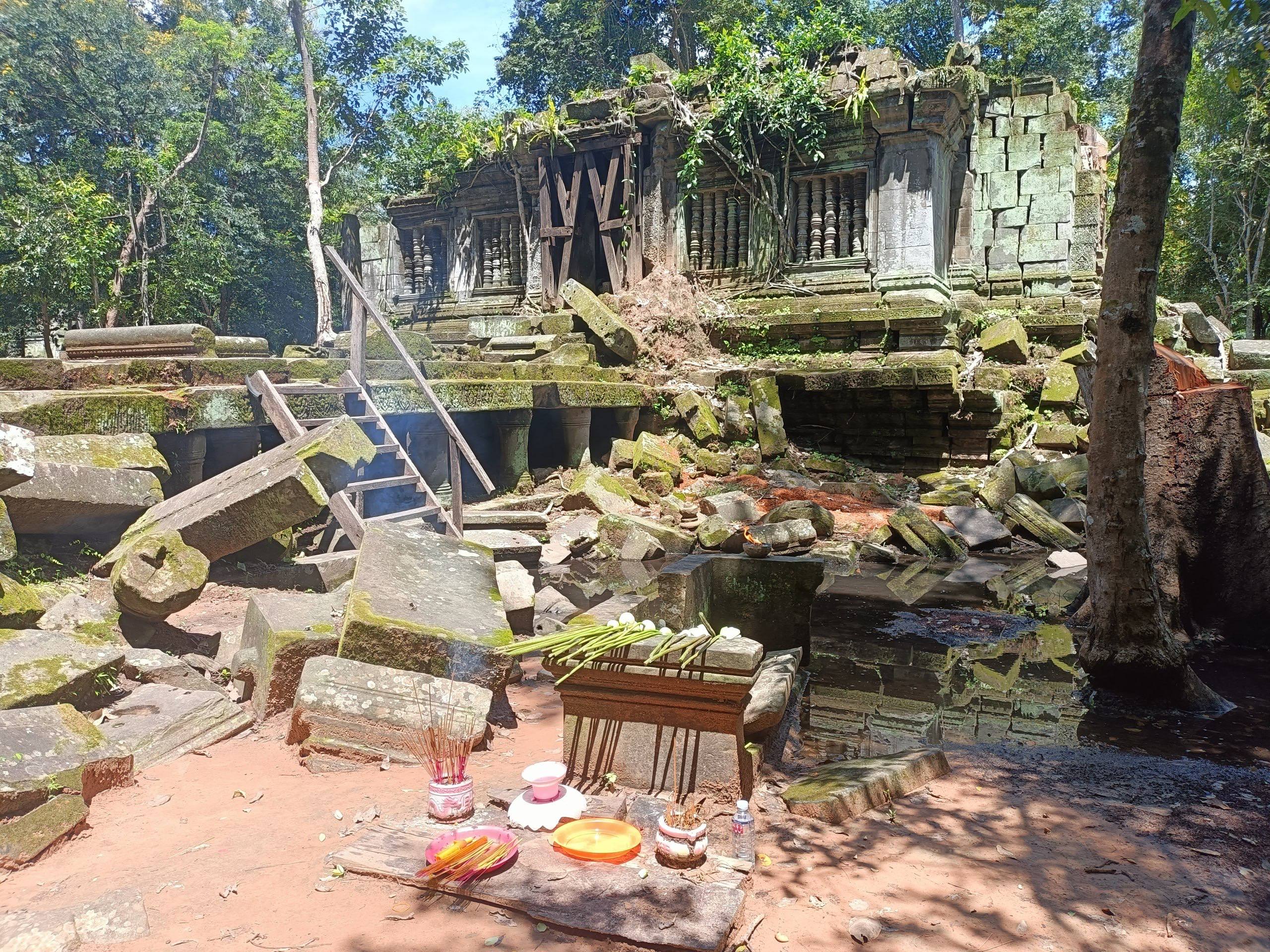Ancient stone ruins of Beng Mealea surrounded by lush jungle and towering trees.